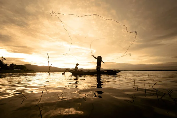 Silhouette Fisherman Fishing by using Net on the boat with sunlight in Thailand, Nature and Culture concept