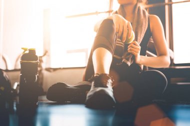 Spor yapan kadın antrenmandan sonra oturup dinleniyor ya da spor salonunda protein içeceği ya da yerde içme suyu ile egzersiz yapıyor. Rahat ol. Kuvvet eğitimi ve Vücut Geliştirme teması. Sıcak ve serin bir ton 