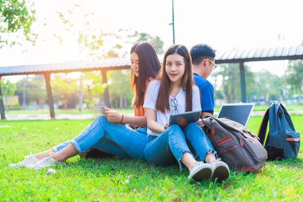 Gruppe von asiatischen College-Studenten mit Tablet und Laptop auf der Wiese im Freien. Technologie und Bildungskonzept. Zukunftstechnologie und modernes Unterhaltungskonzept. Edutainment-Thema. — Stockfoto