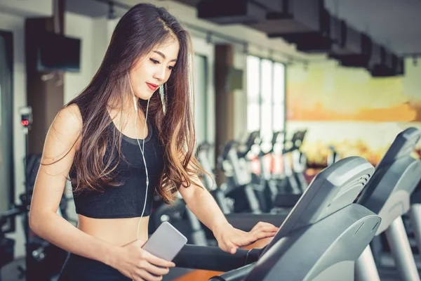 Mulher asiática usando telefone inteligente quando treino ou treinamento de força no ginásio de fitness na esteira. Relaxe e conceito de tecnologia. Exercício desportivo e tema de cuidados de saúde. Humor feliz e confortável . — Fotografia de Stock