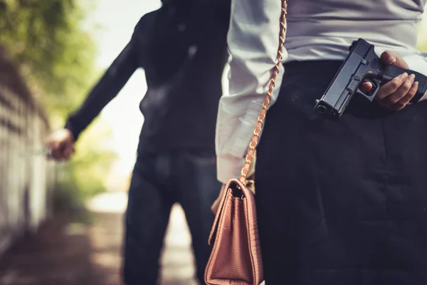Закрыта женщина, прячущая пистолет сзади за драку с грабителем или защиту от кражи денег или опасности. Концепция уголовного и сексуального насилия. Новости и тема экономического спада — стоковое фото
