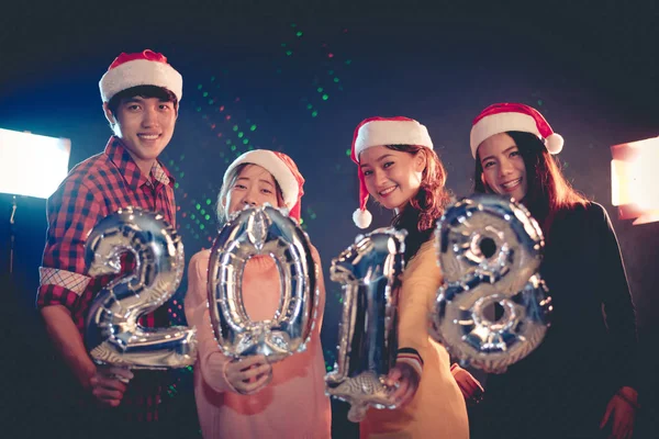 Asian people who wearing Santa hat celebrating New year party 2018 and showing alphabets balloon in night pub or bar. Christmas and New year 2018 concept. Xmas party in nightlife