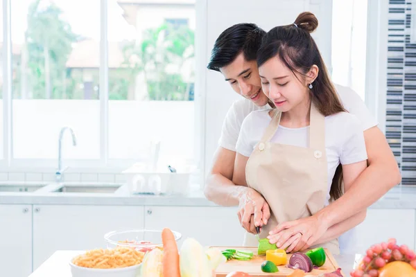 Amantes asiáticos o pareja cocinando y rebanando verduras en la sala de cocina. Hombre y mujer mirándose en casa. Concepto de vacaciones y luna de miel. Día de San Valentín y boda tema — Foto de Stock