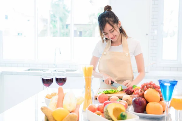 Mujer cocinando y rebanando verduras en la sala de cocina con comida y fruta en la mesa. Concepto de vacaciones y felicidad . — Foto de Stock