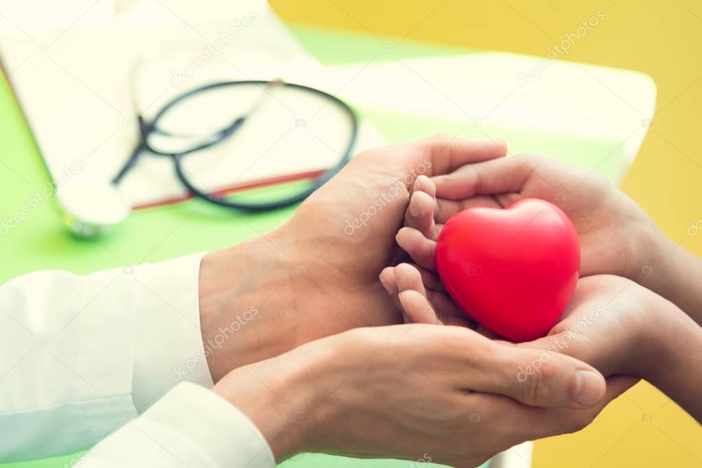 Hand of doctor give red heart to little patient children for rec