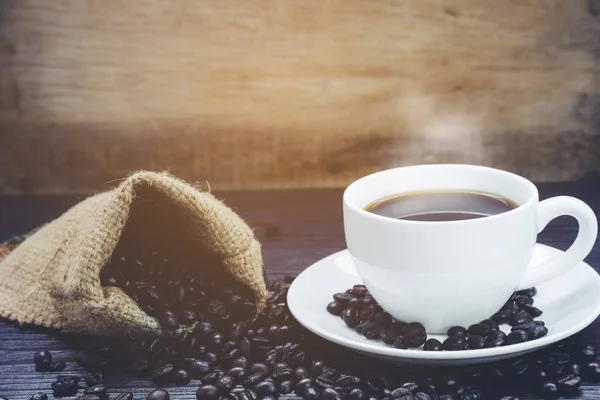 Vista lateral de la taza de café con humo y granos de café en saco en — Foto de Stock