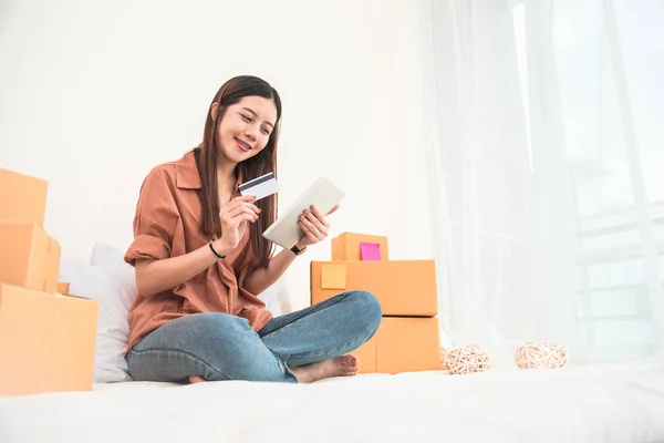 Young Asian woman startup small business entrepreneur SME distribution warehouse with parcel mail box. Owner home office. Online marketing and product packaging and delivery service. Credit card use