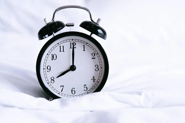 Relógio de alarme preto na cama branca. Conceito de tempo e horas. Interior e objeto tema — Fotografia de Stock