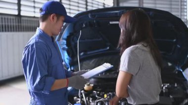 Araç teknisyeni müşteriyle araba tamir masrafları ve sigorta hakkında konuşuyor. Asyalı kadın bakım garajı servis atölyesinde tamirci dinliyor. Otomotiv