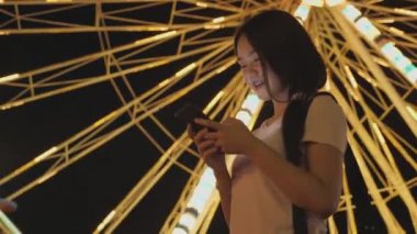 Mutlu Asyalı kadın dönme dolap geçmişiyle lunaparktaki arkadaşlarıyla telefon konuşmalarına bak. İnsanların yaşam tarzı ve eğlencesi. Seyahat ve tatil