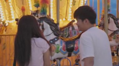 Lunaparkta romantik bir an yaşarken çitin yanında Atlıkarınca 'ya bakan Asyalı çiftin arka plan görüntüsü. İnsanların yaşam tarzı ve tatil seyahati konsepti. Sevgililer günü ve balayı düğünü onları rahatlatır..