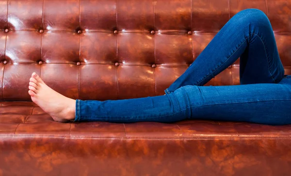 여자들은 영화관이나 집에서 소파에서 휴식을 취하는 청바지를 다리를 벌리고 컨셉트 — 스톡 사진