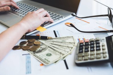 Ofis masasındaki dizüstü bilgisayarla çalışan kadının elini kapat. Kağıt gözlük ve hesap makinesiyle rapor ver. İş ve insanların yaşam tarzları. Finansal ve ekonomik yatırım. Evden çalış.