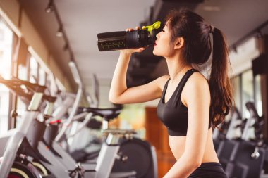 Asyalı güzel bir kadın spor salonunda protein içeceği ya da içme suyu içiyor. Spor ve insanlar konsepti. Spor ve spor teması. Daire ya da apartmanda faaliyet gösteren bir kız