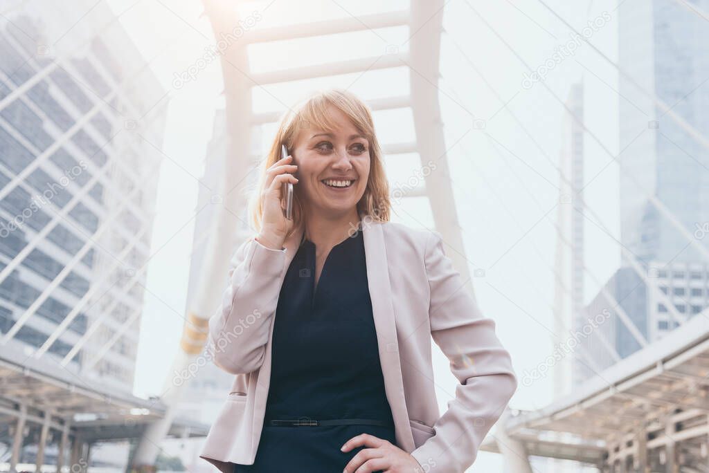 Happy businesswoman using smart phone to commnicate and talk to business agreement in urban city background. People lifestyles and technology concept. Outdoor working and social distancing concept