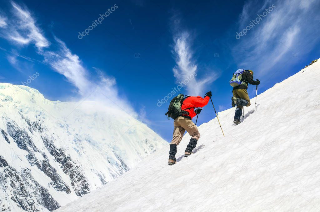 Two mountain trekkers on steep snowed hill with dramatic sky bac