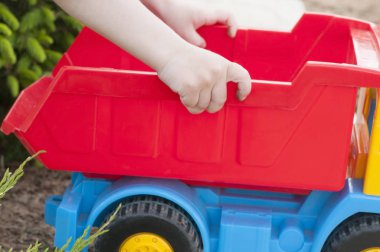 Bir çocuk büyük kırmızı oyuncak araba ile çimenlerin üzerinde oynuyor