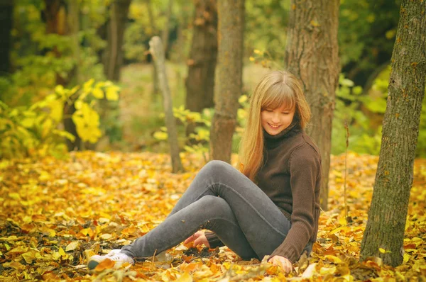 Young girl in autumn forest, throws yellow leaves, toned photo — Stock Photo, Image