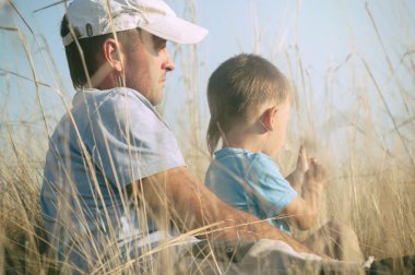 Baba ve oğul alanında oturmuş, baba hugs onun oğlu, tonda fotoğraf