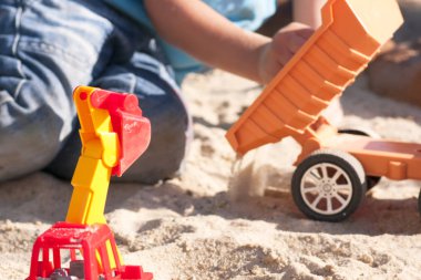 Kum büyük oyuncak arabalar, bir ekskavatör, bir kamyon ile bir çocuk oynar