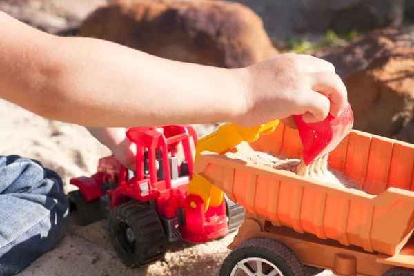 Kum büyük oyuncak arabalar, bir ekskavatör, bir kamyon ile bir çocuk oynar