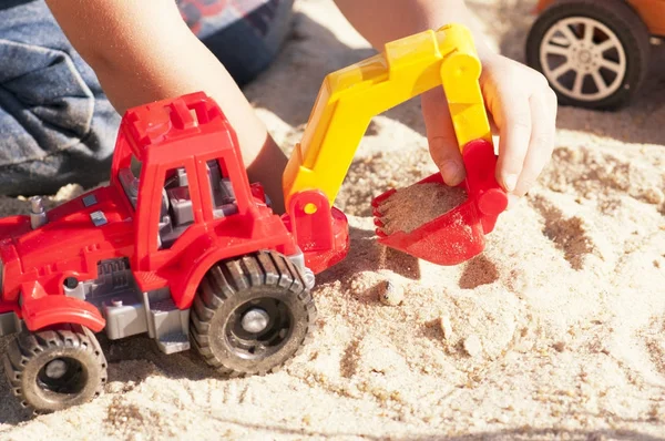 Kum büyük oyuncak arabalar, bir ekskavatör, bir kamyon ile bir çocuk oynar