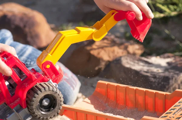 Kum büyük oyuncak arabalar, bir ekskavatör, bir kamyon ile bir çocuk oynar