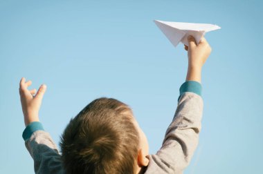 Bir çocuk bir oyuncak kağıt uçak alanında mavi gökyüzü ile oynuyor