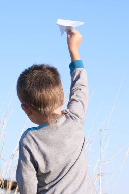 Bir çocuk bir oyuncak kağıt uçak alanında mavi gökyüzü ile oynuyor