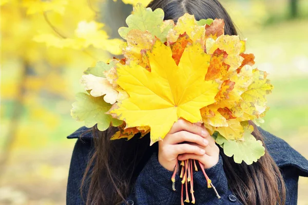 Girl hides her face behind yellow autumn leaves, bouquet, autumn