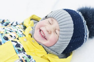 Little boy playing in the snow, portrait, lying on his back, laughing
