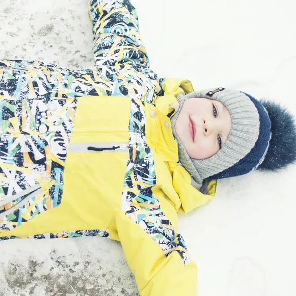 Little boy playing in the snow, portrait, lying on his back, laughing