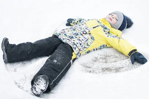 A child, a boy, lies on the snow, makes a snow angel with his arms and legs, emotions, laughs — Stock Photo, Image