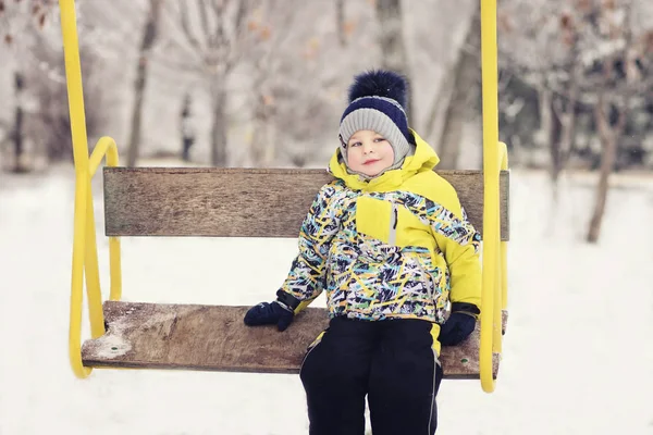 Het kind. jongen in winterkleren rijden op een schommel, emotie, lachen, winter, sneeuw — Stockfoto