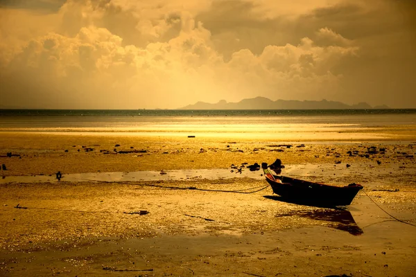 A small boat on the beach at sunset. The sun is setting, there is golden light on the water. — Stock Photo, Image