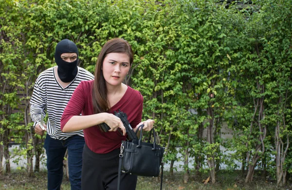 Чоловік-розбійник стоїть і дивиться на молоду жінку і молоду жінку, яка бере пістолет у свою сумочку/самозахист жінки, кримінальна концепція — стокове фото