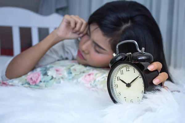 Азиатка на белой кровати проснулась поздно. Посмотри на будильник. — стоковое фото