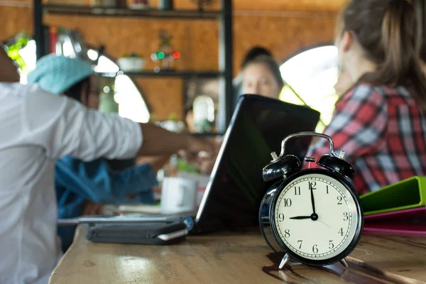 Reloj despertador en mesa de madera con fondo abstracto borroso de discusión de negocios grupo de personas o equipo de reunión — Foto de Stock