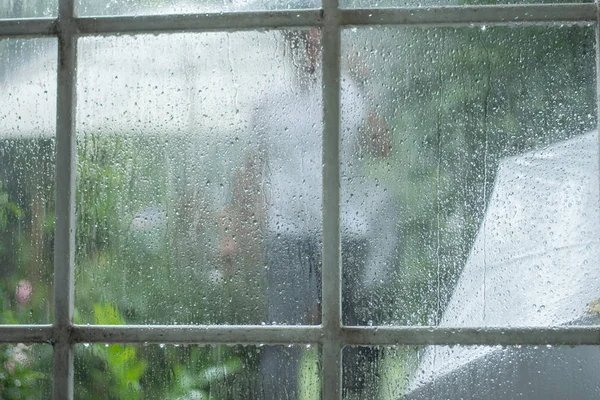 Pencere camına yağmur damlaları ile görülen şemsiyesi altında adamlardan bulanık soyut — Stok fotoğraf