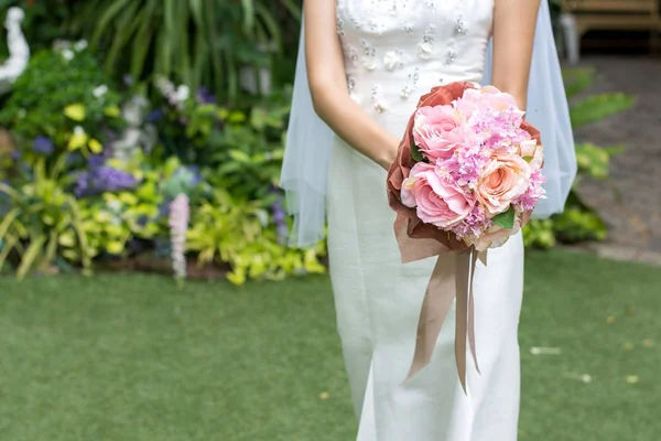 Невеста в белом платье держит свадебный букет цветов с лентами — стоковое фото