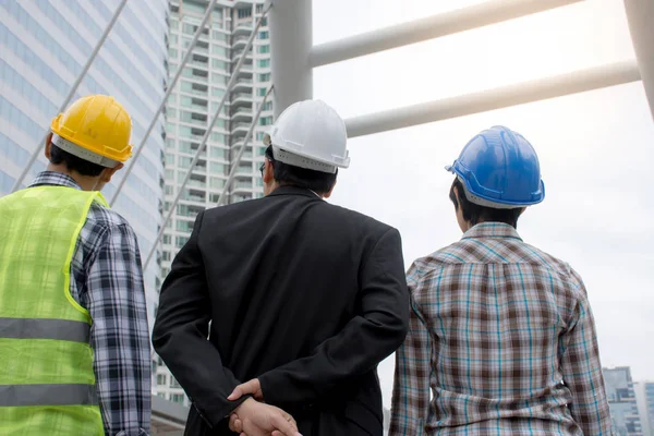 Blick von hinten auf das asiatische Ingenieursteam, das einen Schutzhelm trägt und über Bauvorhaben spricht — Stockfoto