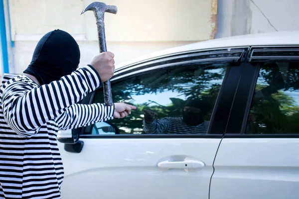 The man robber with a balaclava on his head holding a hammer trying to break into the car/Selective focus/Criminal and car thief concept