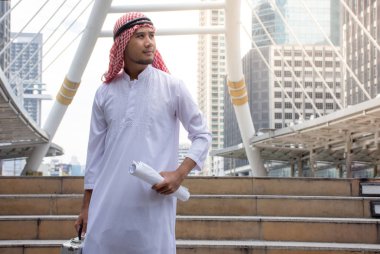 Arap işadamı blueprint ve Evrak Çantası'nı hissediyorum emin ve şehir arka plan ile başarılı holding