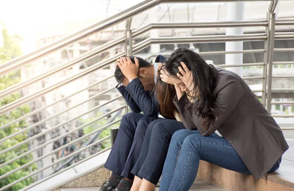 Portrait of stressed business team holding hands on her head with headache and sitting at the stairs having problems.