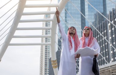 İki Arap işadamı buluşup birlikte konuşurken tartışmıyoruz evrak çantası şehir arka plan/iş kavramı ile tutarak parmak işaret eden oktan yukarı bilgi formları. 