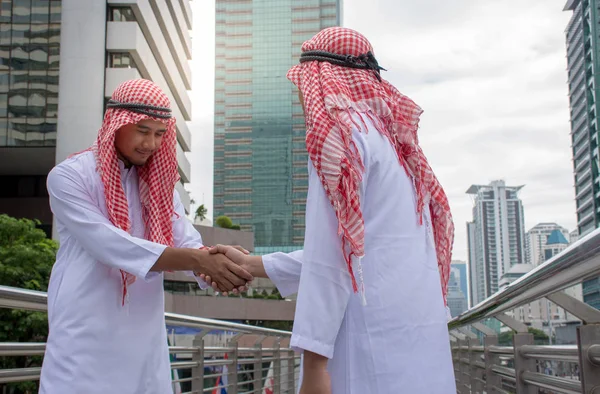 Arabic business people shaking hands over a deal negotiation to success with city background