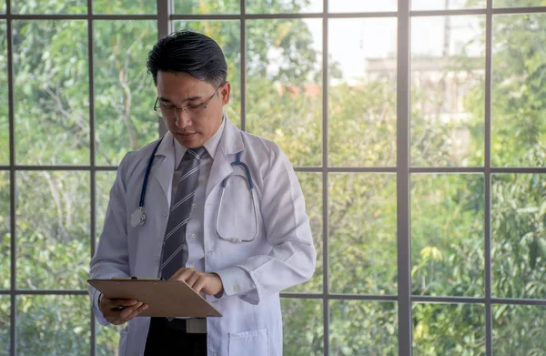 Asian doctor discuss documentation at a hospital with blurred window background/Copy space in right side