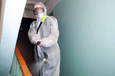 Koronavirüsteki bir evin girişinde insan sterilizasyon uygular. Enfeksiyonlar, böcekler veya fareler koruyucu tulum giyer.