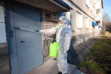 Koronavirüsteki bir evin girişinde insan sterilizasyon uygular. Enfeksiyonlar, böcekler veya fareler koruyucu tulum giyer.