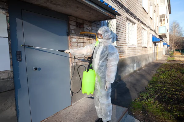 Koronavirüsteki bir evin girişinde insan sterilizasyon uygular. Enfeksiyonlar, böcekler veya fareler koruyucu tulum giyer.